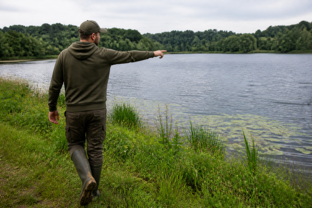 Pêcheur de carpe marchant sur les berges d'un étang et pointant une zone profonde